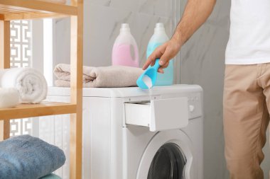 Çamaşır deterjanı banyodaki çamaşır makinesinin çekmecesine dolduran adam.