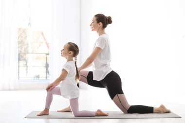 Küçük kızı olan genç bir anne evde yoga yapıyor.