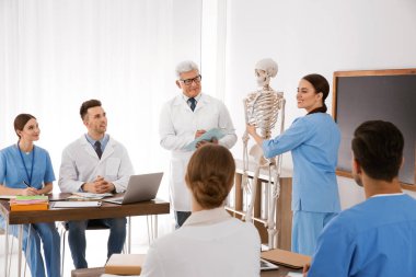 Tıp öğrencileri ve profesör sınıfta insan iskeleti anatomisi okuyor.