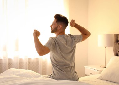 Young man stretching on bed at home. Lazy morning