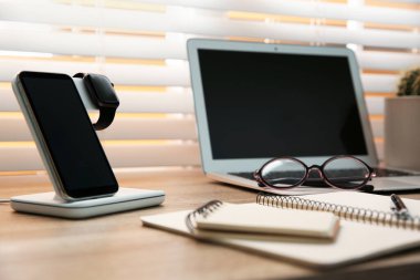 Cep telefonu ve ahşap masada kablosuz şarj aleti olan akıllı bir cihaz. Modern işyeri aksesuarı