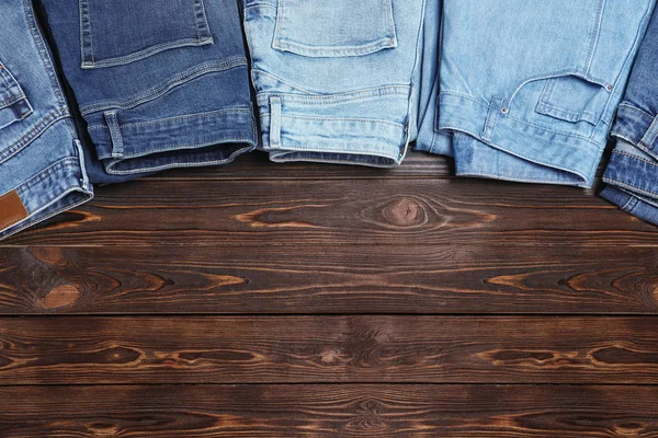 Collection of stylish jeans on wooden background, flat lay. Space for text