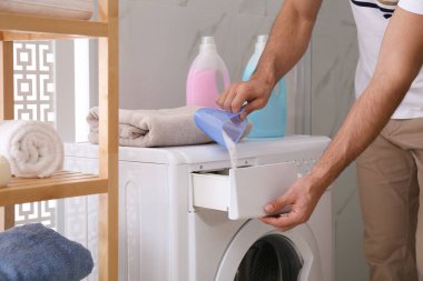 Çamaşır deterjanı banyodaki çamaşır makinesinin çekmecesine dolduran adam.
