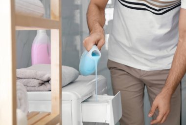 Banyodaki çamaşır makinesi çekmecesine deterjan döken adam, yakın plan. Çamaşır günü