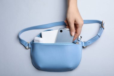 Açık gri arka planda, küçük çantadan akıllı telefonu alan kadın.