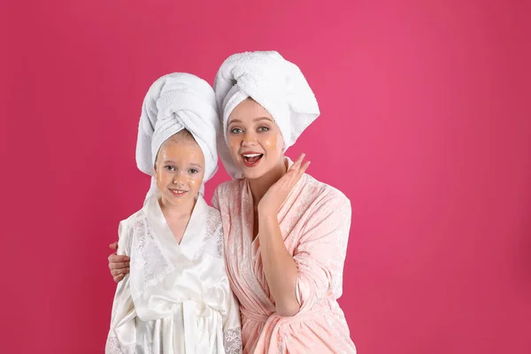 Emotional mother and daughter with facial masks on pink background