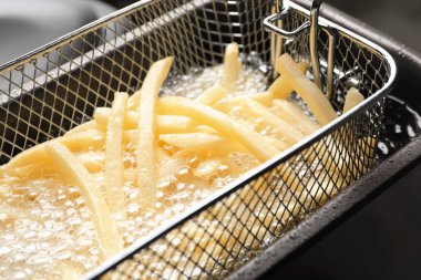 Cooking delicious french fries in hot oil, closeup clipart