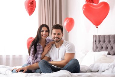 Yatak odasında kalp şeklinde balonlarla süslenmiş genç bir çift. Sevgililer Günü kutlaması