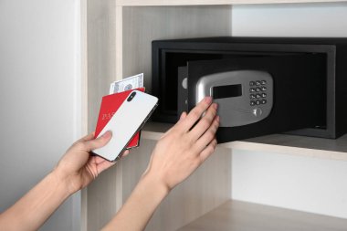 Akıllı telefonu, pasaportu ve parayı çelik kasaya koyan kadın, yakın plan.