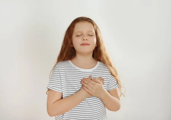 Schattig Dankbaar Klein Meisje Met Handen Borst Tegen Lichte Achtergrond — Stockfoto