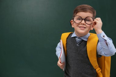 Kara tahtanın yanında gözlük takan şirin bir çocuk. Mesaj için yer var. Okula ilk gelişim.