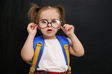 Cute little child wearing glasses near chalkboard. First time at school
