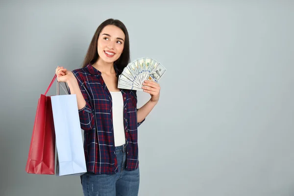 Young woman with money and shopping bags on light grey background. Space for text