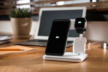 Cep telefonu, kulaklıklar ve ahşap masada kablosuz ped ile şarj olan akıllı sehpa. Modern işyeri aygıtı