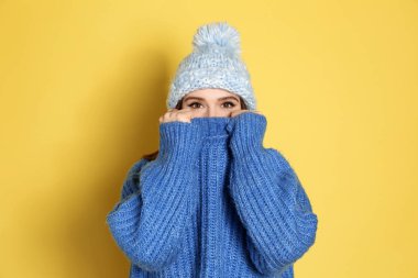 Sarı arka planda kalın kazak ve şapka giyen genç bir kadın. Kış mevsimi