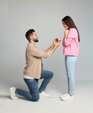 Nişan yüzüklü bir adam açık gri arka planda kız arkadaşına evlenme teklif ediyor.