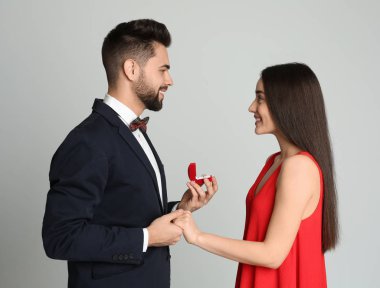 Nişan yüzüklü bir adam açık gri arka planda kız arkadaşına evlenme teklif ediyor.