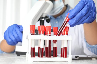 Bilim adamı laboratuardaki raftan kan örneğiyle test tüpü alıyor. Yakın plan. Virüs araştırması
