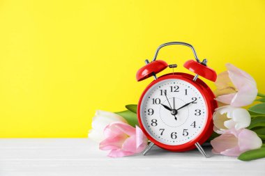 Kırmızı alarm saati ve sarı arka planda bahar çiçekleri, mesaj için yer. Zaman değişimi