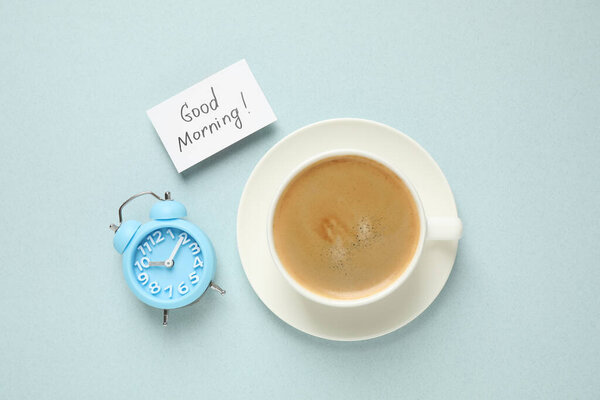 Delicious coffee, alarm clock and card with GOOD MORNING wish on light background, flat lay