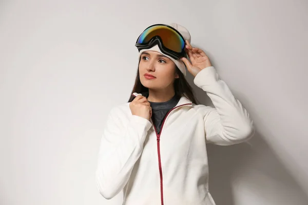 Woman wearing fleece jacket and goggles on light grey background. Winter sport clothes