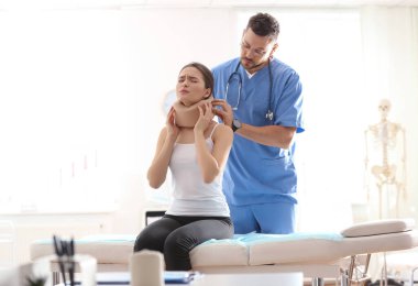 Erkek ortopedist klinikteki hastanın boynuna boyun tasması takıyor.