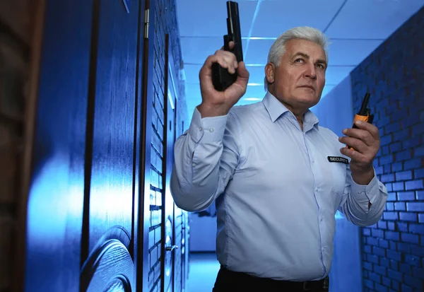 Professional security guard with gun and portable radio set in dark hallway