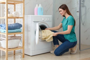 Banyoda çamaşır makinesinin yanında elbiseleri olan genç bir kadın. Çamaşır günü