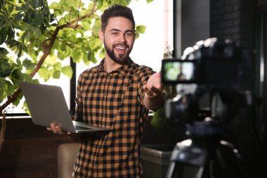 Bilgisayarlı genç blogcu içeride video kaydediyor.