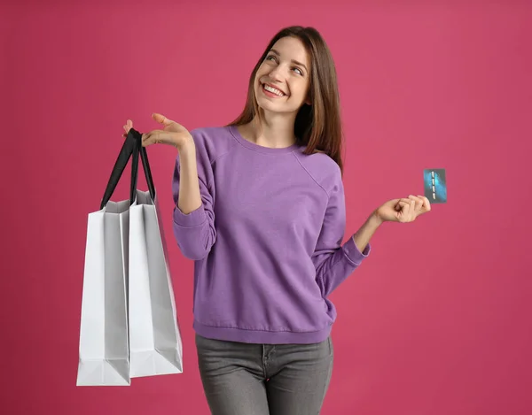 快乐的年轻女人 有信用卡和粉色背景的购物袋 支出款项 — 图库照片