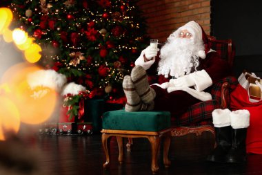 Noel Baba bir bardak sütle Noel ağacının yanındaki koltukta dinleniyor.