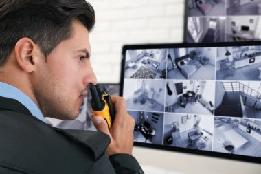 İş yerindeki monitörlerin yanında taşınabilir vericisi olan erkek güvenlik görevlisi.