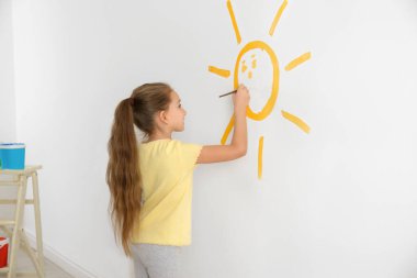 Küçük çocuk beyaz duvarlara güneş çiziyor.
