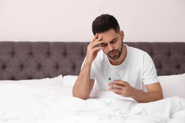 Young man addicted to smartphone in bed at home