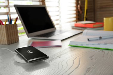 Beyaz ahşap masada kablosuz şarj aleti olan bir cep telefonu. Modern işyeri aksesuarı