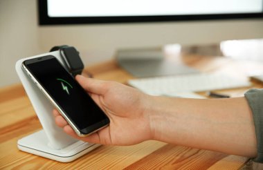 Ahşap masadaki kablosuz şarj cihazından cep telefonunu alan adam, yakın plan. Modern işyeri aksesuarı