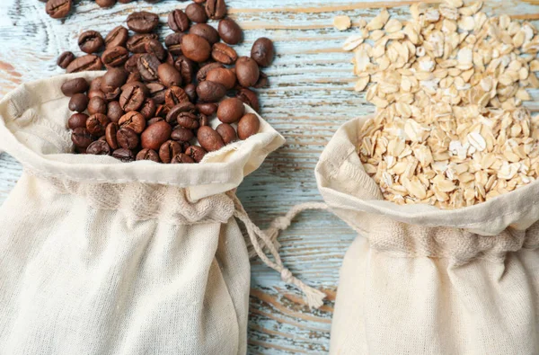 Cotton eco bags with oat flakes and coffee beans on wooden table, flat lay