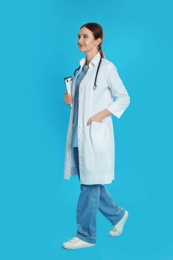 Mavi arka planda yürüyen, klipsli ve steteskoplu bir doktor.