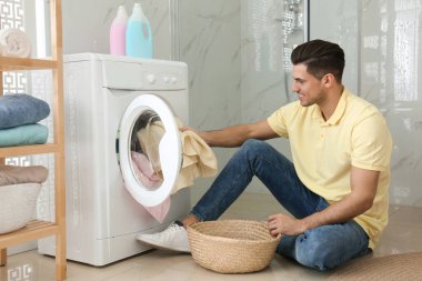 Adam banyodaki çamaşır makinesine çamaşır koyuyor. Çamaşır günü