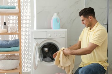 Banyoda çamaşır makinesinin yanında giysileri olan bir adam. Çamaşır günü