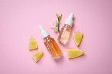 Flat lay composition with bottles of citrus essential oil on pink background