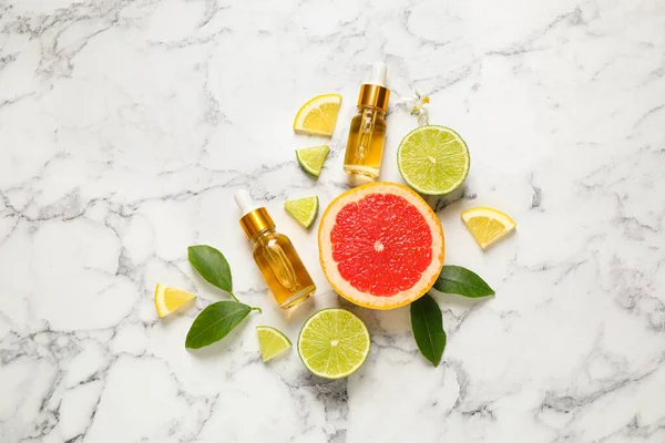 Flat lay composition with bottles of citrus essential oil on white marble background