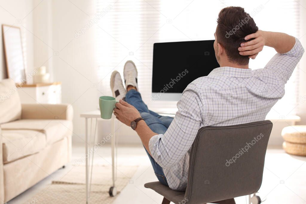 Young man with cup of drink relaxing at table in office during break