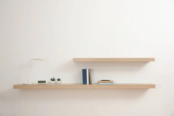 Wooden shelves with books and decorative elements on light wall