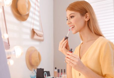 Güzel genç bir kadın soyunma odasında aynanın yanında makyaj yapıyor.