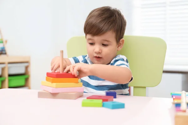 Little child playing with toy pyramid at table