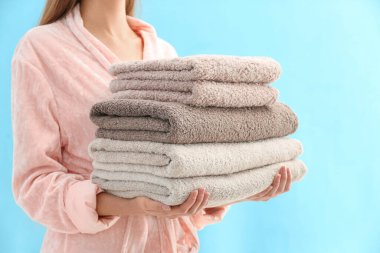 Woman holding stack of fresh clean towels on light blue background, closeup