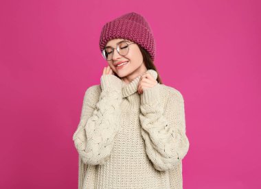 Kızıl arka planda kalın kazak ve şapka giyen genç bir kadın. Kış mevsimi