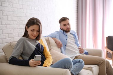 Genç adam evde kız arkadaşının akıllı telefonuna bakıyor, kadına odaklanıyor. İlişki sorunları