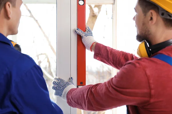 Workers using bubble level for installing window indoors, closeup